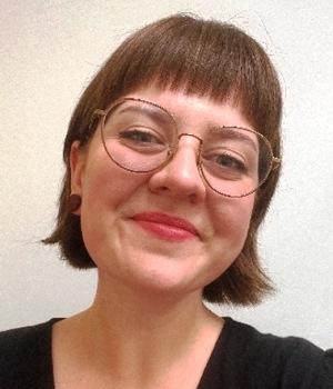 Smiling brown-haired woman wearing a dark top and light-framed glasses